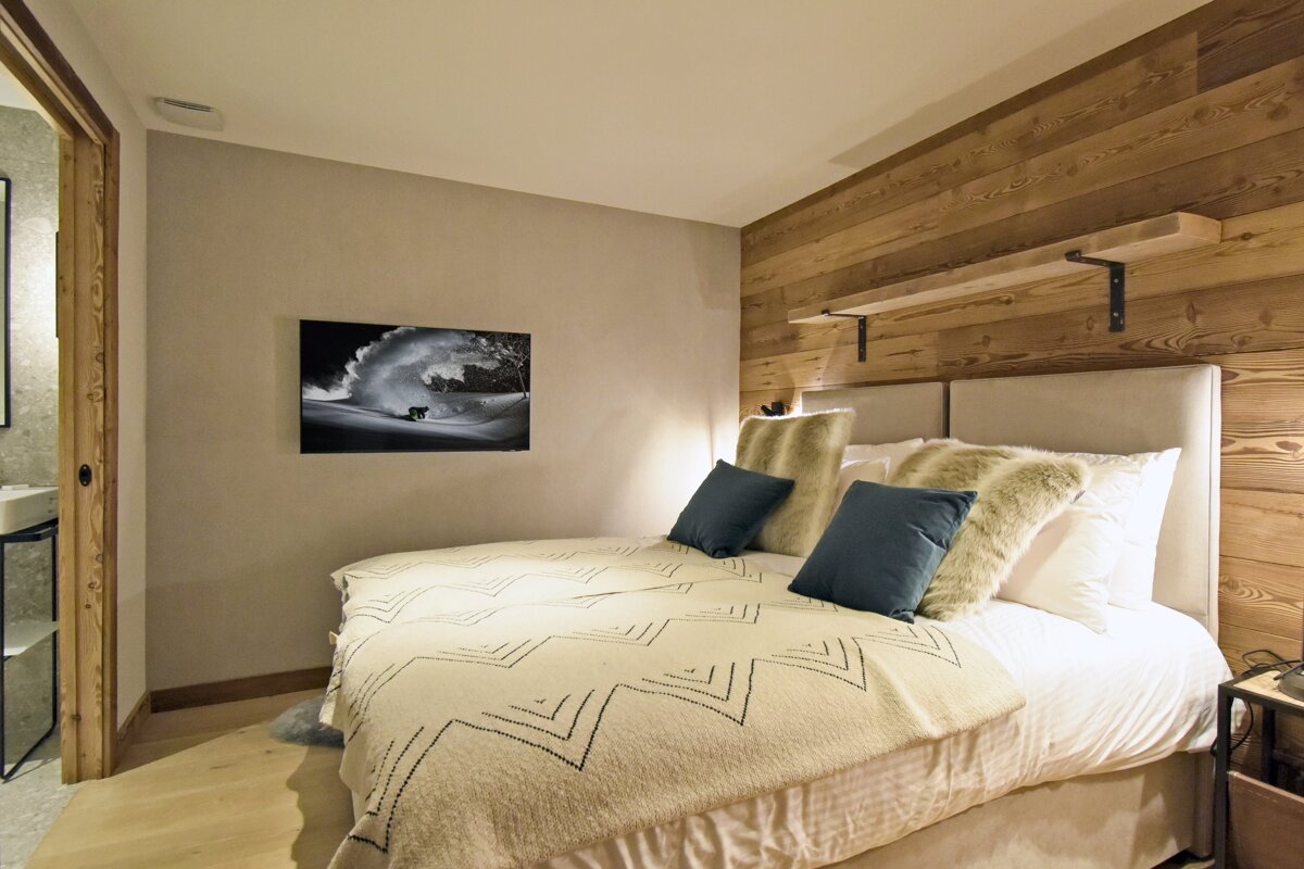 Cozy chalet bedroom featuring a wood-paneled wall, a bed with patterned blanket and plush pillows, and a black-and-white print.