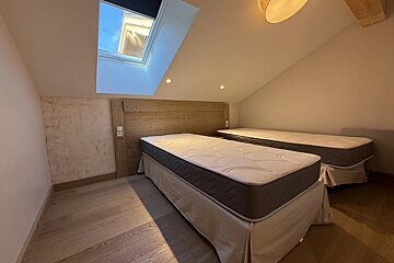 Two single beds with a wooden headboard in an attic bedroom featuring a sloped ceiling, a skylight, and light wood flooring.