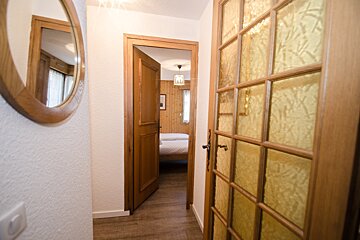 A hallway leading to a bedroom with a bed and a mirror