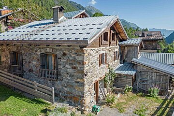 A stone house with a metal roof and mountains in the background