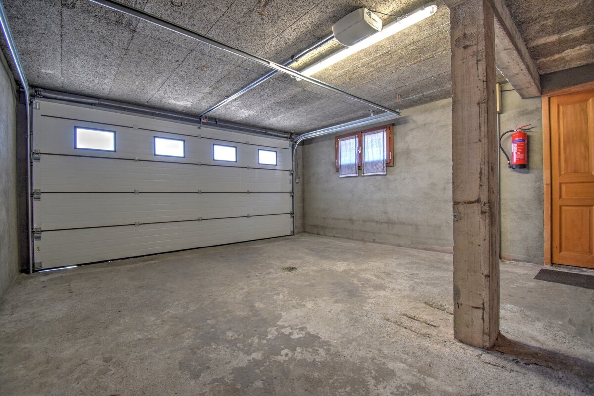 An empty concrete garage featuring a large white sectional door, a concrete support pillar, a small window, and a red fire extinguisher.