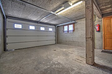 An empty concrete garage featuring a large white sectional door, a concrete support pillar, a small window, and a red fire extinguisher.
