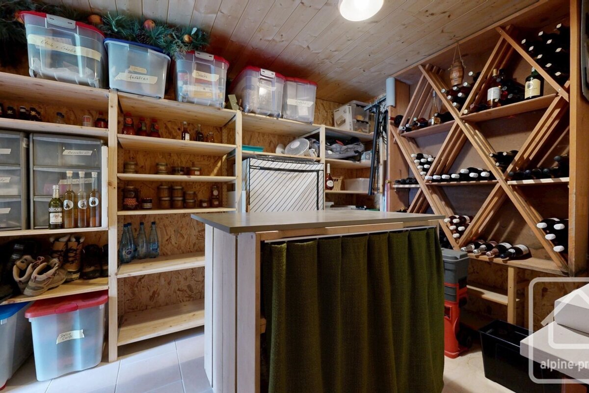 An organized wooden storage room featuring extensive shelving for pantry items, clear containers, and a large wine rack filled with bottles.