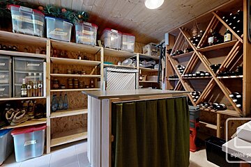 An organized wooden storage room featuring extensive shelving for pantry items, clear containers, and a large wine rack filled with bottles.