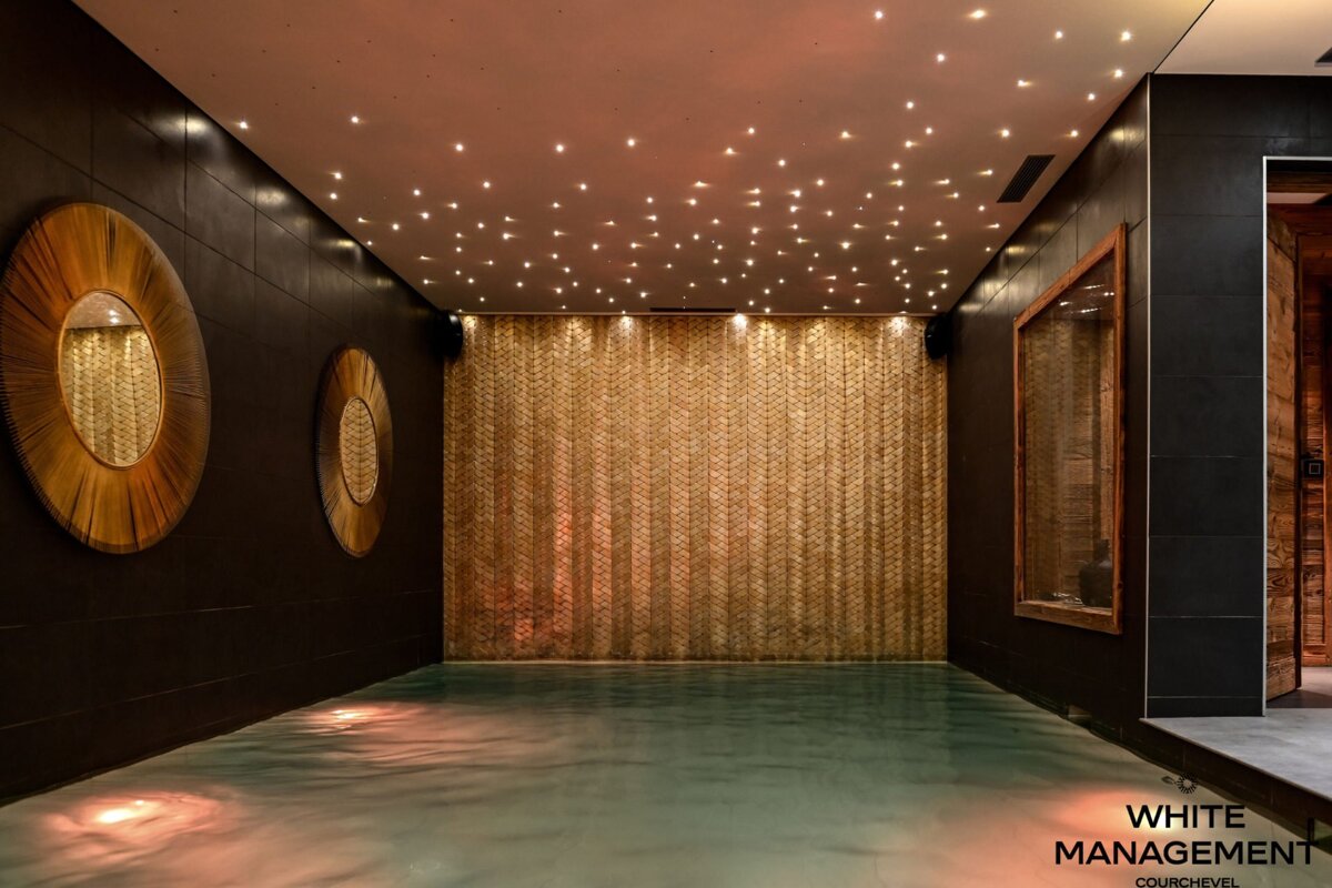 Luxury indoor spa pool with dark tiled walls, decorative round mirrors, a textured gold wall, and a starry light ceiling.