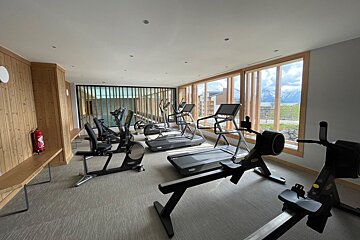 Modern fitness room with treadmills, stationary bikes, and rowers facing large windows with a mountain view.