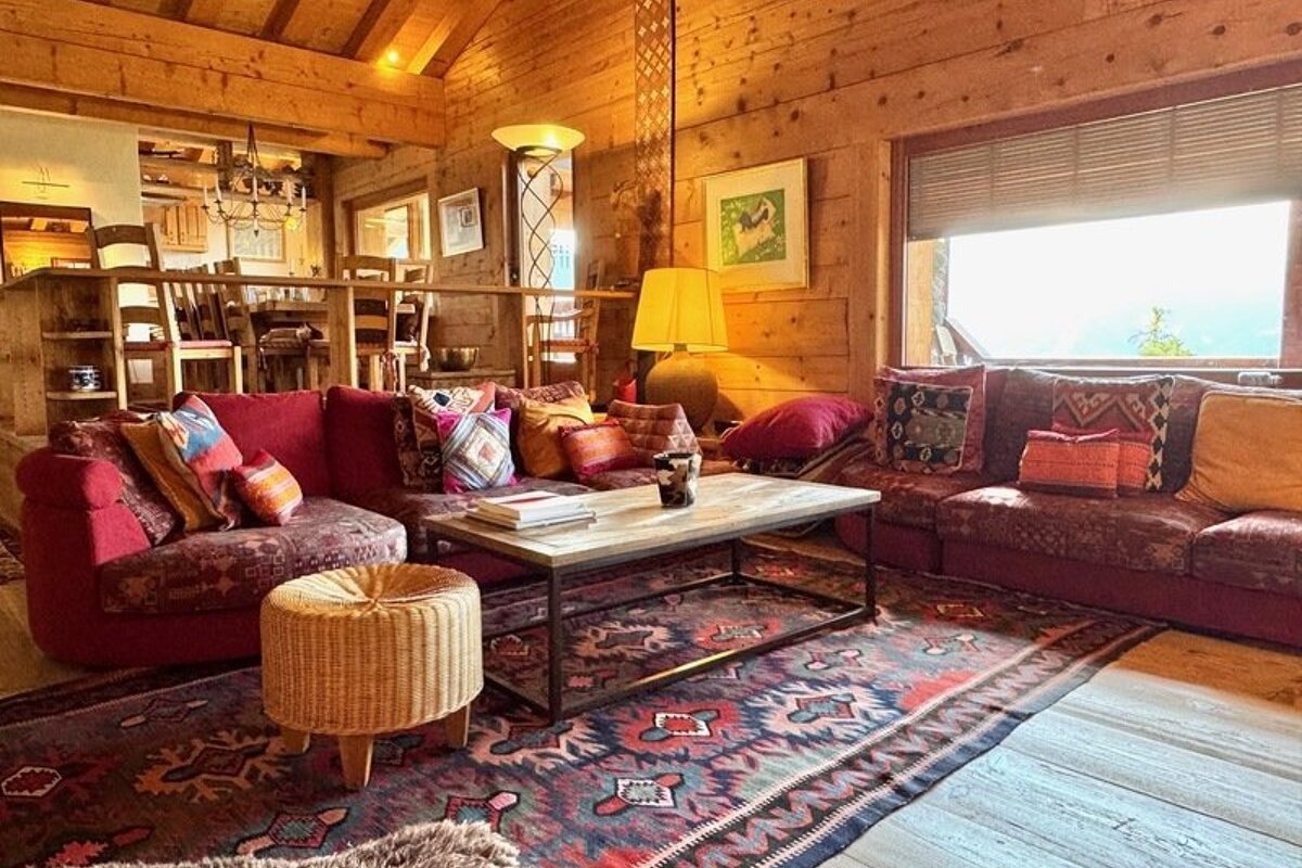 Cozy, rustic cabin living room with red patterned sofas, a wooden coffee table, a large patterned rug, and warm wooden walls.