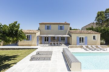 A house with blue shutters sits next to a swimming pool