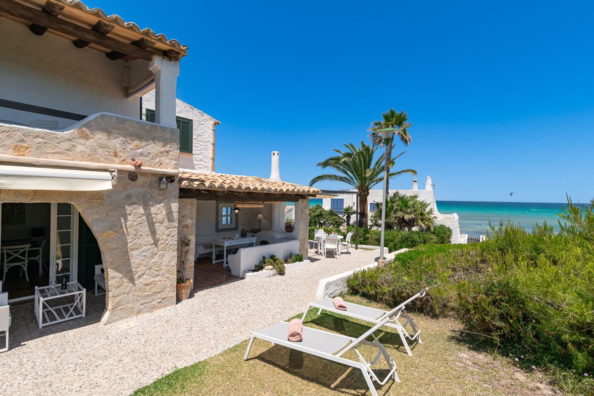Two lounge chairs sit in front of a house overlooking the ocean