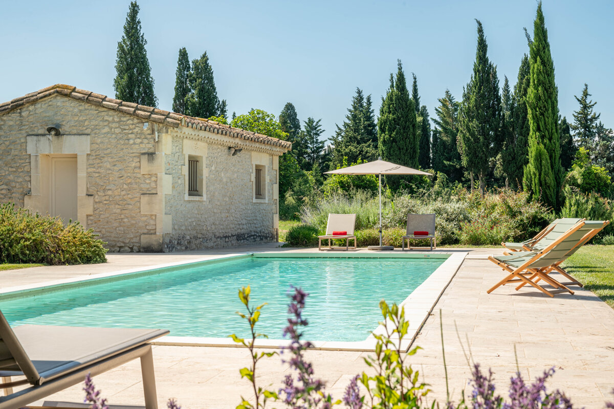 A swimming pool with chairs and an umbrella in front of a stone building