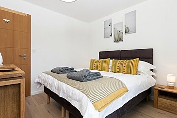 A modern bedroom featuring a bed with yellow accent pillows, polar bear wall art, and warm wooden furniture.