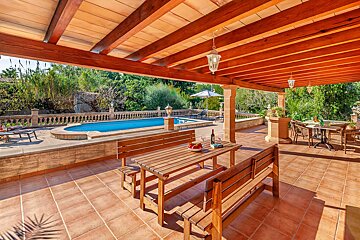 A wooden table with a bowl of fruit on it sits under a wooden roof