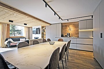 Modern open-concept dining room and kitchen featuring a large marble table, grey chairs, sleek cabinetry, and warm wood accents.