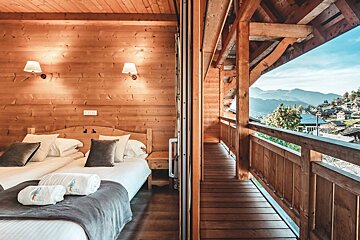 A bedroom with two beds and a balcony with mountains in the background
