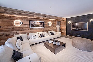 Cozy, modern chalet living room with wood paneling, a large white sectional sofa, coffee table, and TV on a dark accent wall.