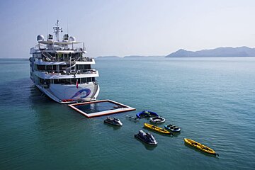 A large yacht with jet skis and kayaks in front of it