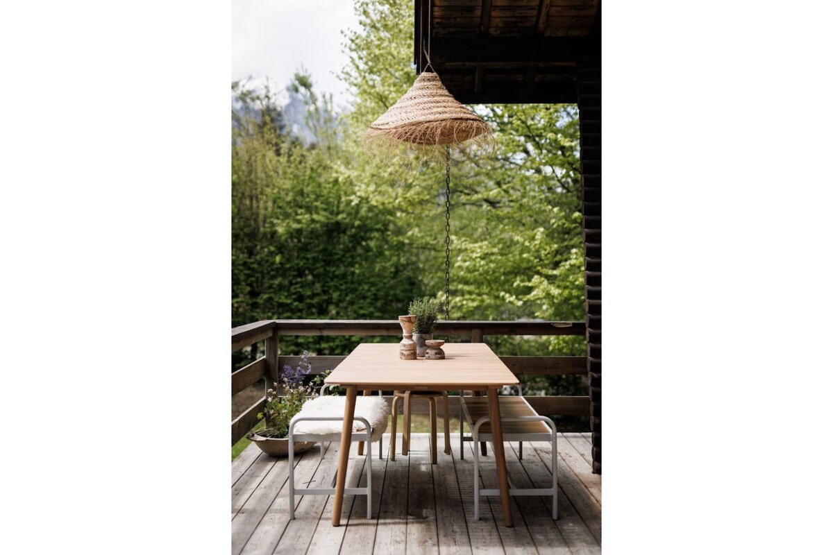 A wooden table and bench on a deck with trees in the background