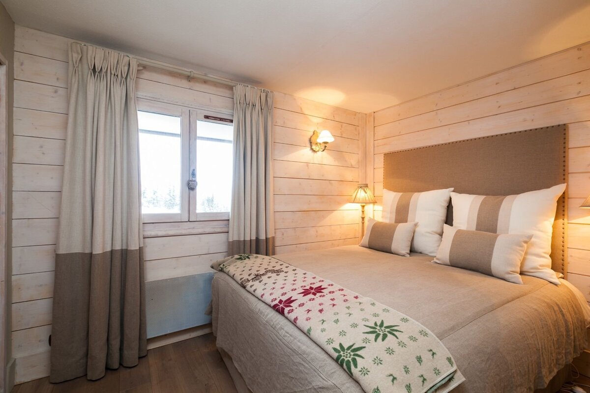 Cozy bedroom featuring whitewashed wood paneling, a large bed with a decorative throw, and warm ambient lighting.