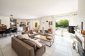 Bright open-plan living room with dining area, brown sofas, and a view of a patio with a swimming pool.