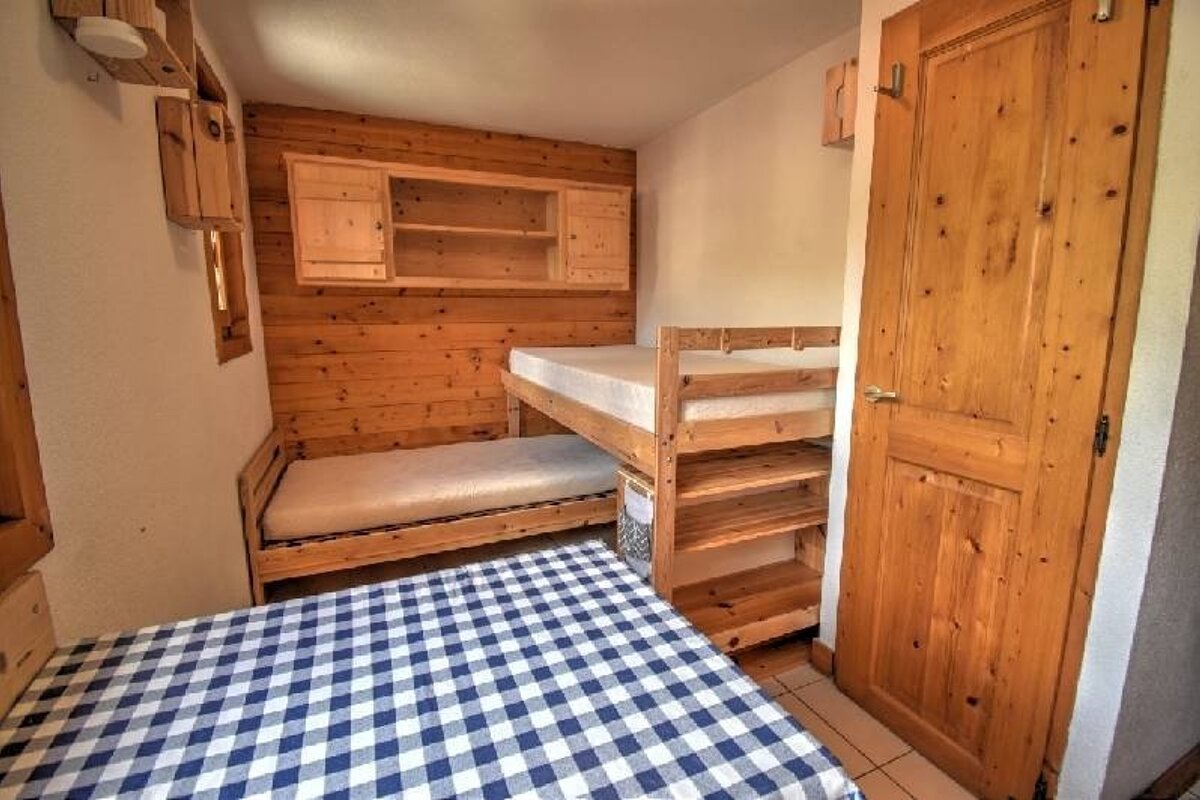 A cozy cabin bedroom featuring wooden walls, a bunk bed, and a bed in the foreground with a blue and white checkered blanket.