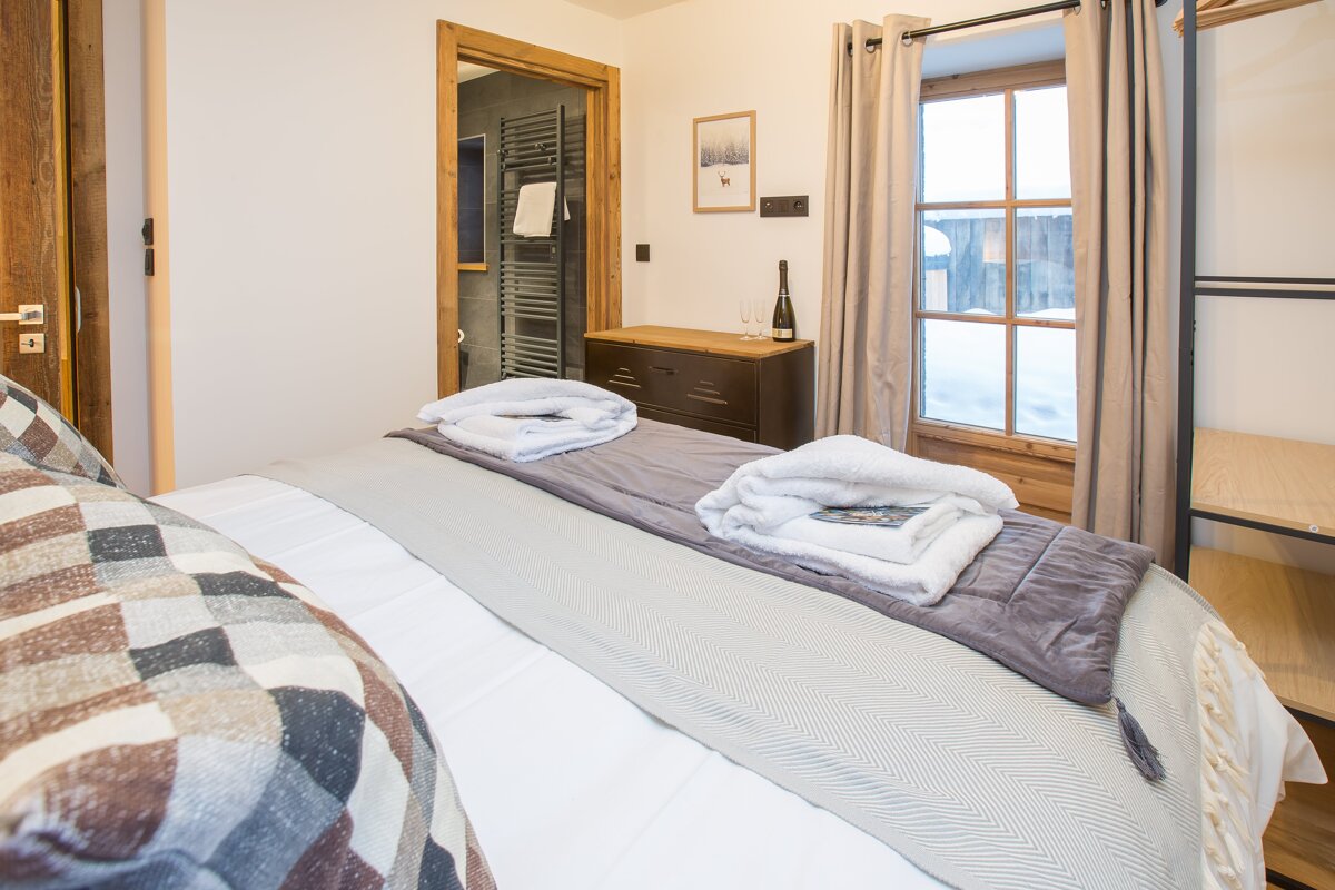 A bedroom with a bed and a dresser with a bottle of wine on it