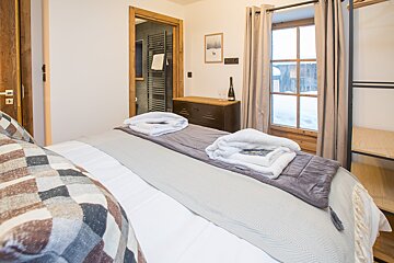 A bedroom with a bed and a dresser with a bottle of wine on it