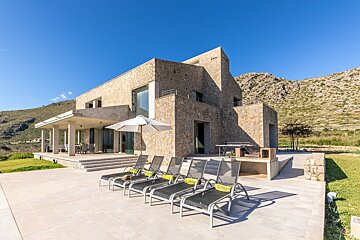 A row of lounge chairs are lined up in front of a large stone house