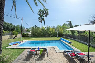 A large swimming pool is surrounded by lawn chairs and a white umbrella