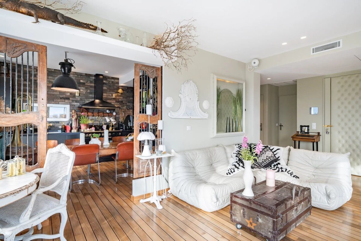 Eclectic open-plan living room and kitchen/dining with white modular sofa, wood floors, vintage trunk, and unique decor including an alligator sculpture.