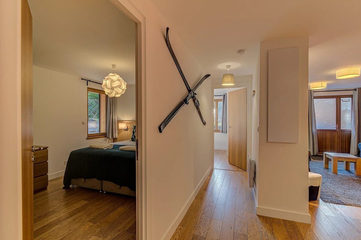 Chalet hallway with wooden floors, crossed vintage skis on the wall, and an open doorway showing a cozy bedroom.