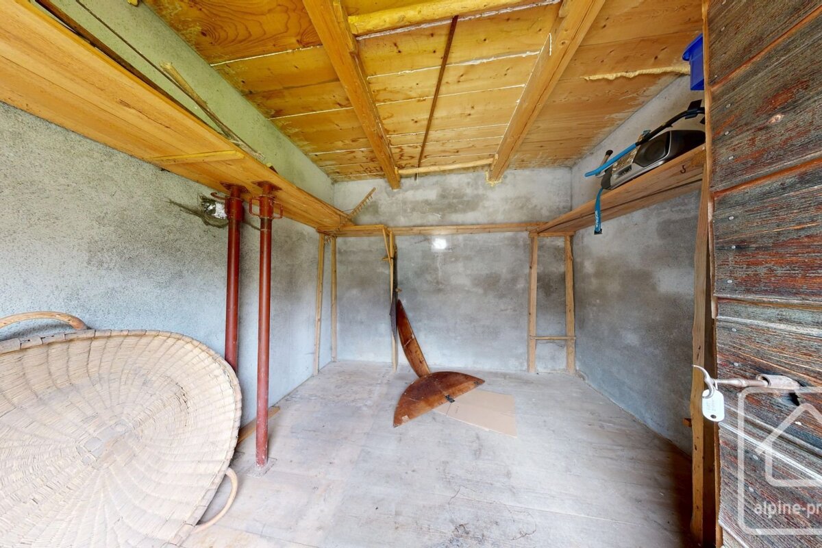 Rustic storage room with concrete walls, wooden ceiling, red support poles, an open wooden door, and a large woven basket.