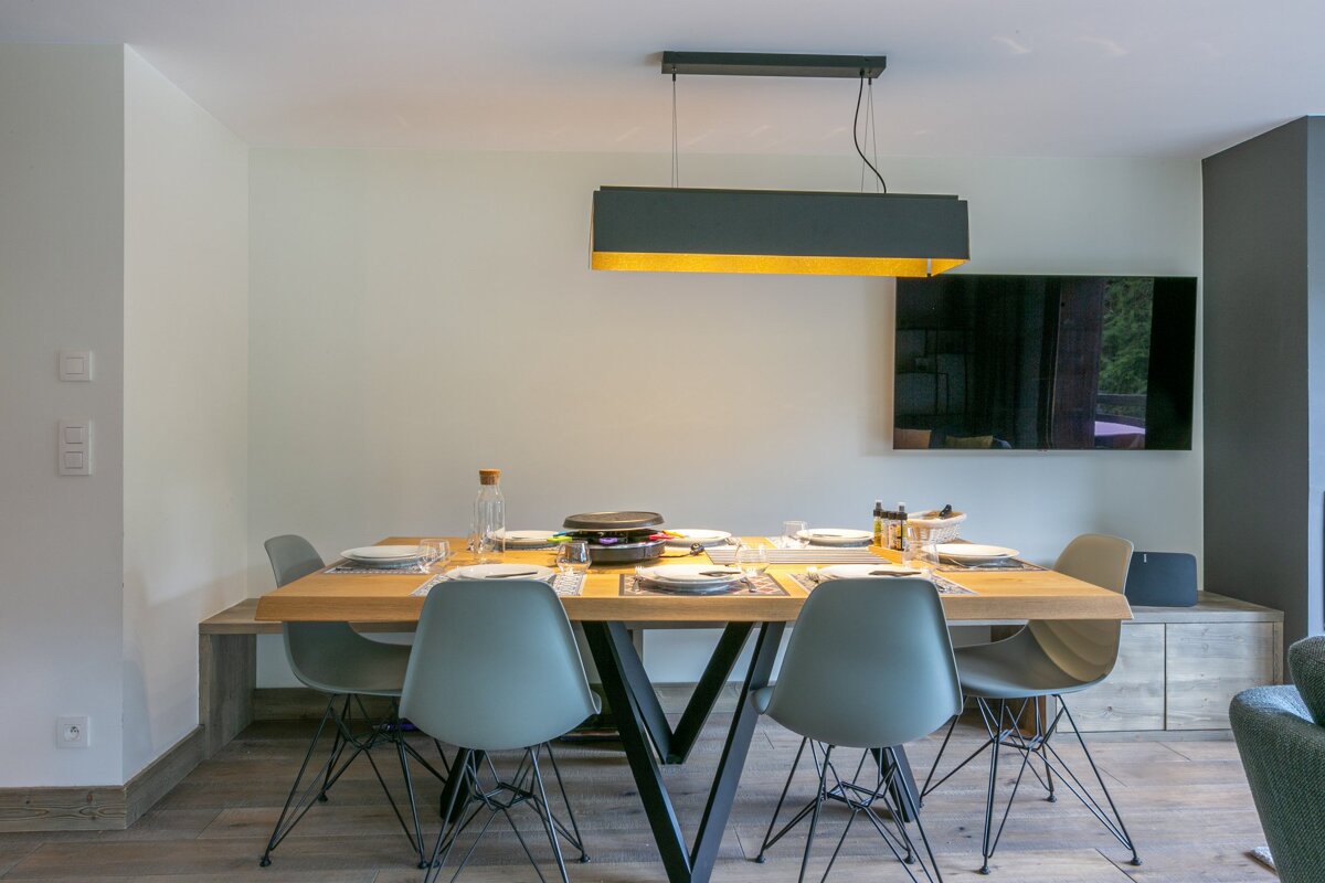 A modern dining room featuring a wooden table set for a meal, four grey chairs, and a sleek black pendant light hanging above.