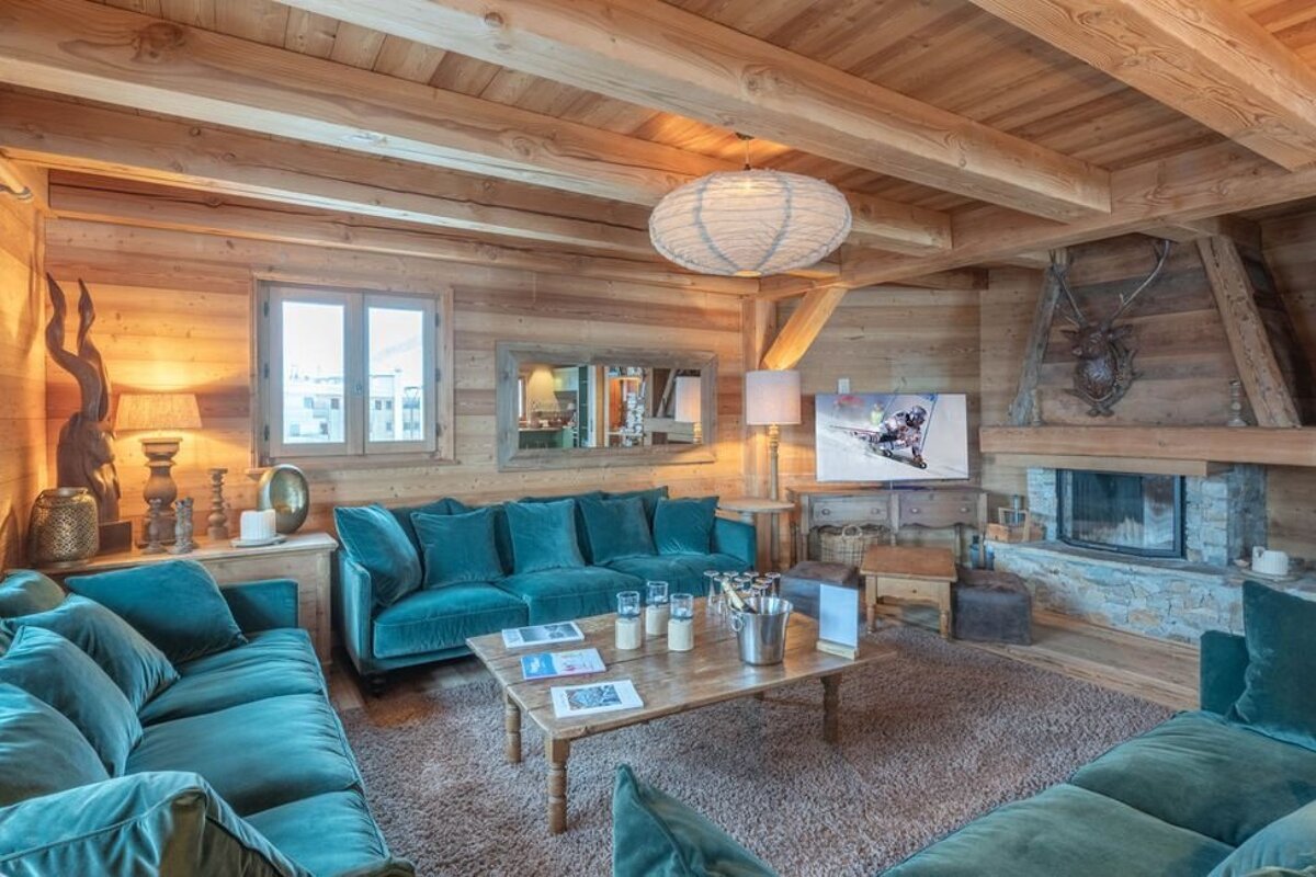 Cozy chalet living room with rustic wood walls, plush teal velvet sofas, and a warm stone fireplace.