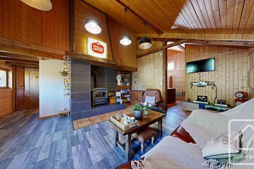 A cozy, wood-paneled living room with a fireplace, TV, sofas, and a Stella Artois sign, creating a rustic chalet feel.