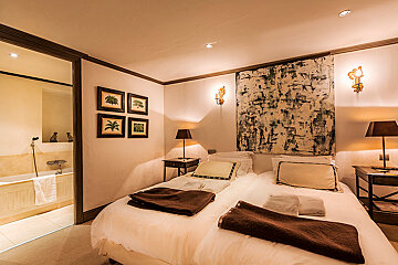 A bedroom with a painting on the wall above the bed