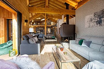 Cozy chalet living room featuring exposed wooden beams, plush sofas, a fireplace, and warm rustic decor.