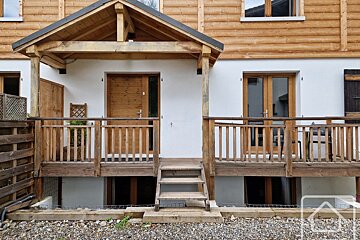 The front of a wooden chalets house with steps, white walls and gravel on the ground.