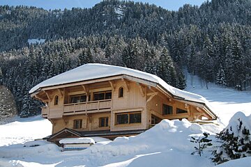 A wooden house is covered in snow in the mountains