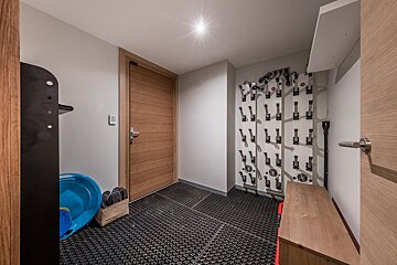 A modern mudroom/ski room with a wooden door, extensive boot drying racks, and a textured black floor, designed for winter gear.