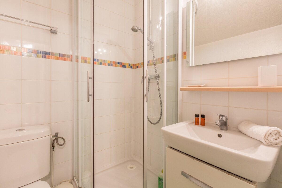 Bright, tiled bathroom with a glass shower, toilet, and modern sink. Colorful mosaic accent stripe runs across the white walls.