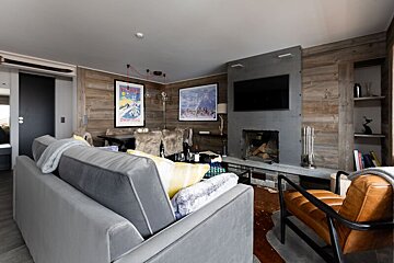 Cozy alpine chalet living room with wood-paneled walls, a grey sofa, a leather armchair, and a fireplace.