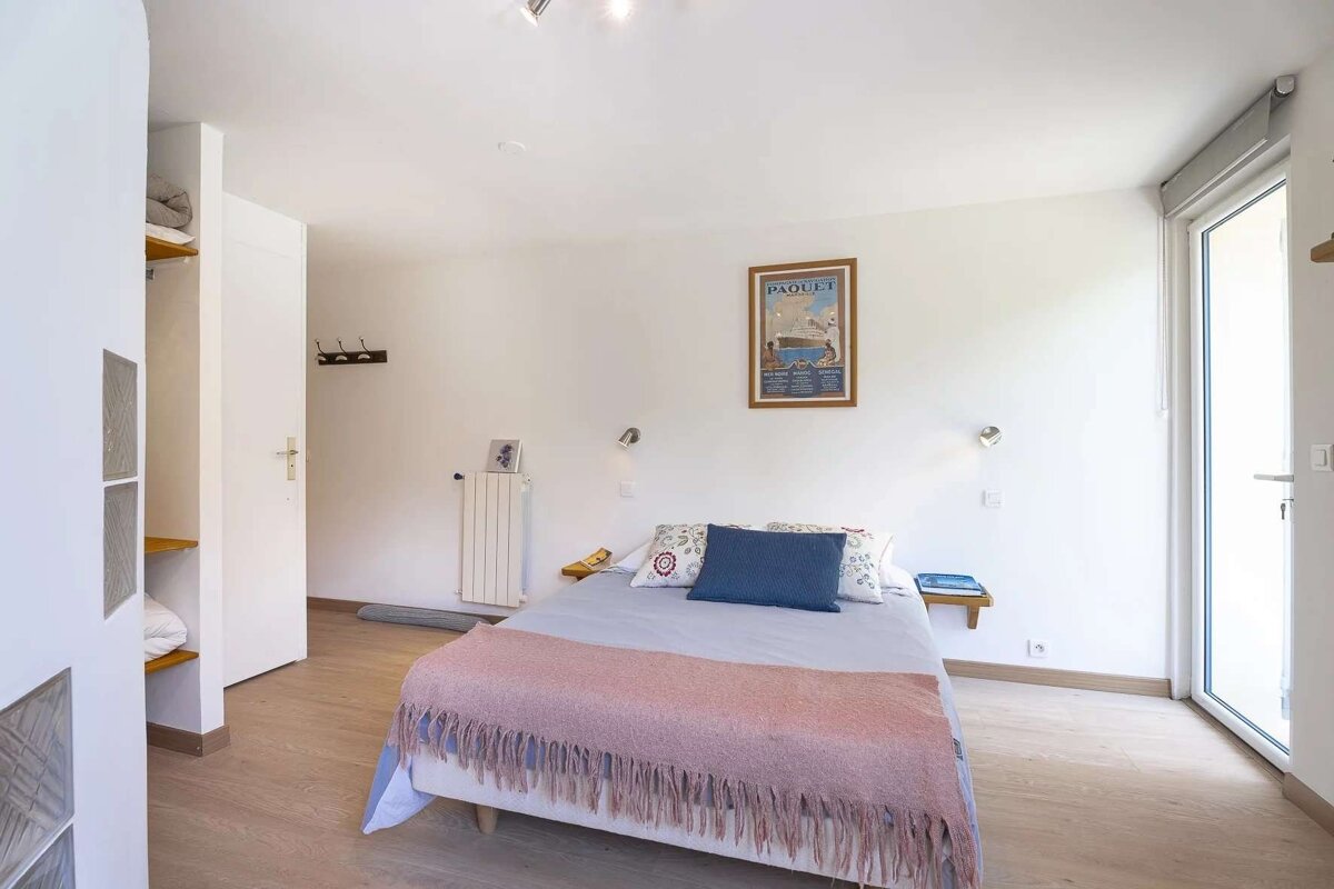 Bright bedroom with a bed, white walls, light wood floor, vintage poster, and a glass door.