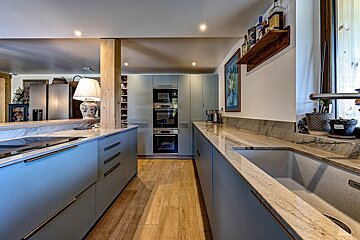 Modern kitchen featuring light blue cabinets, marbled countertops, built-in appliances, and a wooden floor, with an island and bar area.