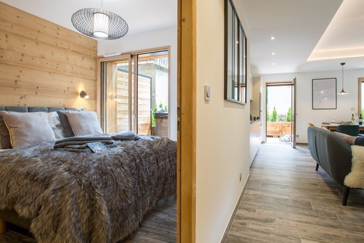 Cozy bedroom with a wooden accent wall and faux-fur blanket, next to a hallway leading into a modern living area.