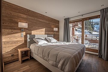 Cozy alpine bedroom featuring a wood-paneled wall, a double bed, and glass doors opening to a snowy balcony view.