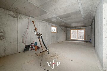 Unfinished concrete room under construction with exposed wiring, a support prop, and wooden-framed windows.