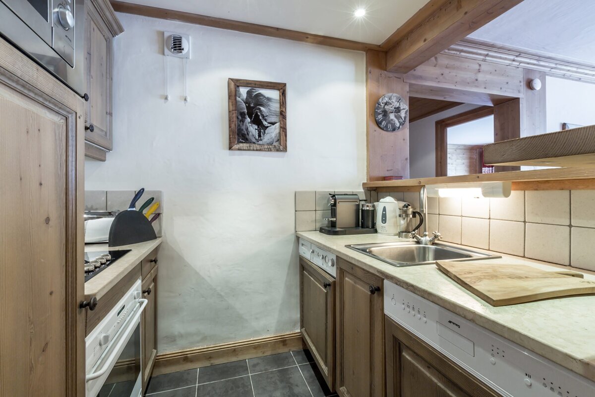 Cozy cabin-style kitchen featuring rustic wooden cabinetry, a stainless steel sink, tiled backsplash, and dark tiled flooring.