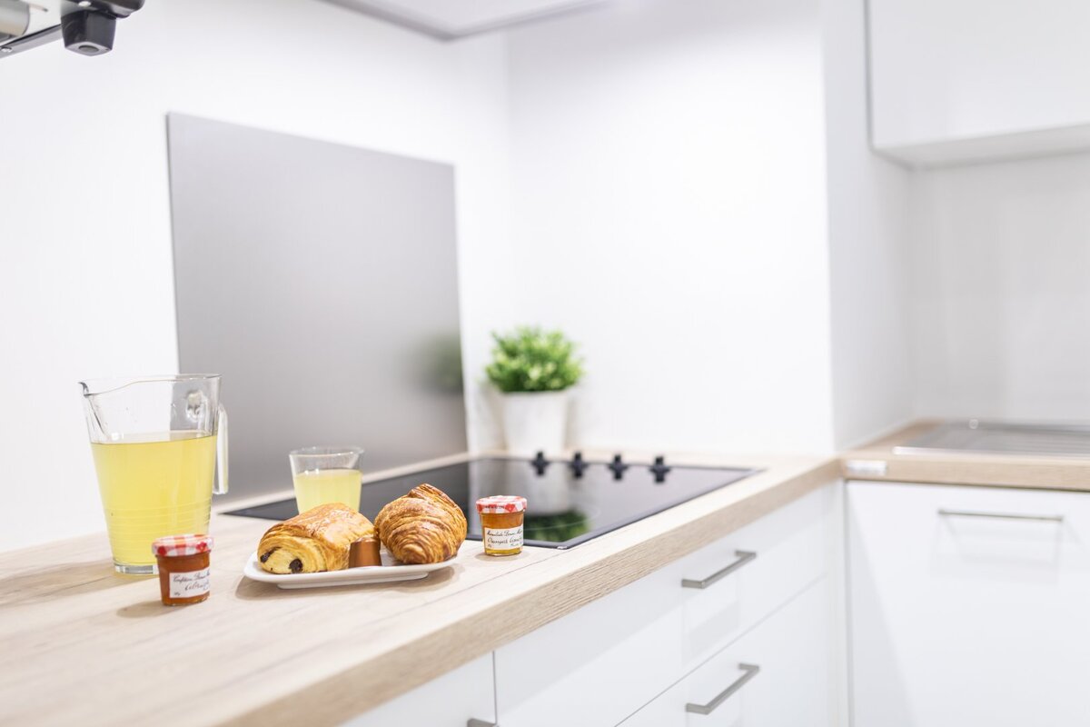 A kitchen counter with a pitcher of lemonade croissants and jars of jam