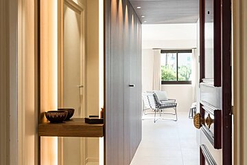 Modern home entryway with wood paneling, warm strip lighting, and a view into a bright living room with chairs.