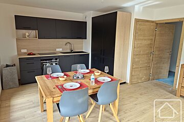 A modern kitchen and dining area featuring dark cabinets, a wooden dining table with set places, and light wood flooring.